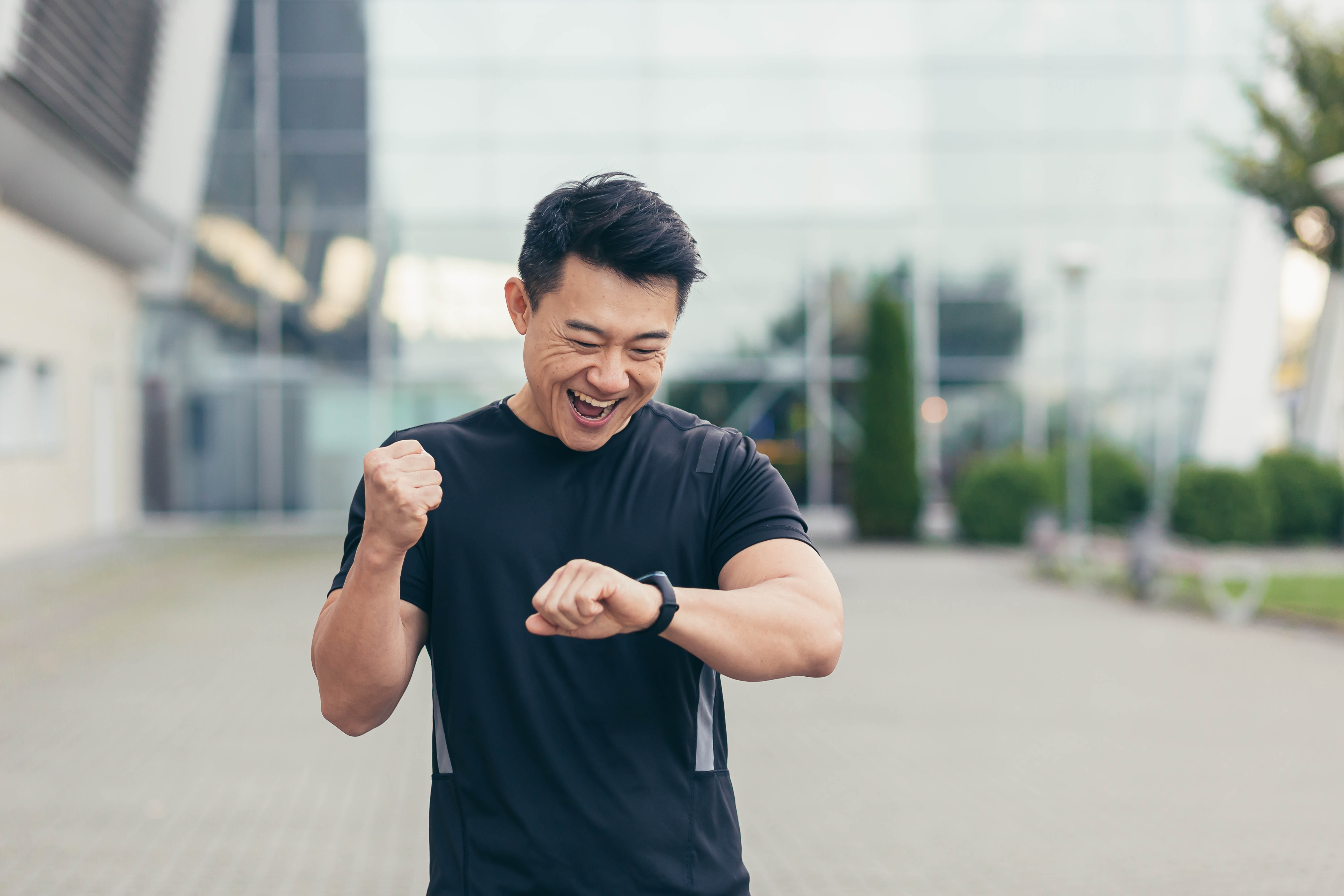 Excited young Asian man looking at his fitness watch and throwing his fist in the air in excitement